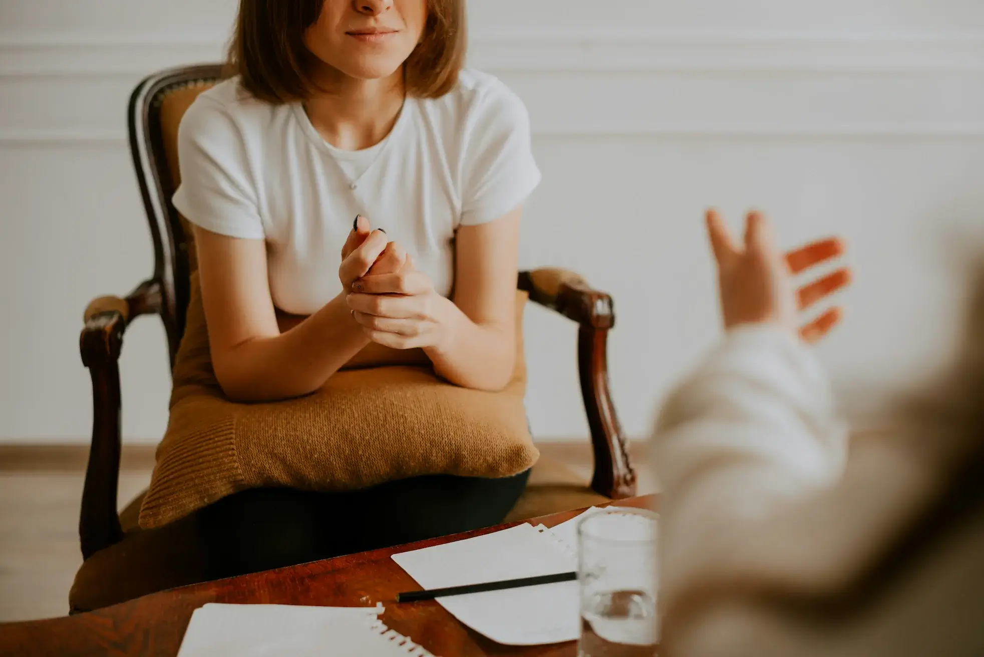 Two people sit across from each other at a table—papers, a pen, and water between them—as a psychiatrist from Rediscovered Psychiatry, New York, listens attentively.