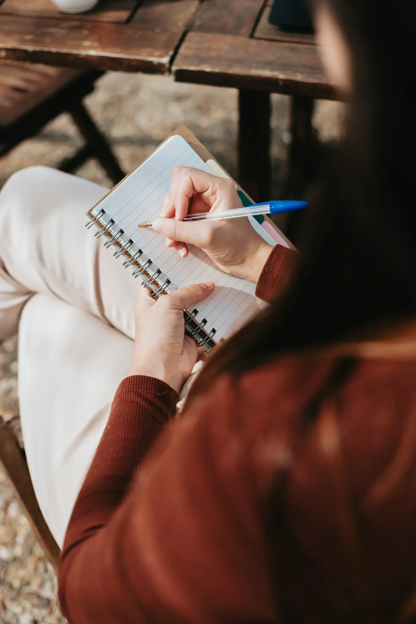 A person sits outdoors in Connecticut, holding a notebook and writing with a pen—perhaps jotting insights inspired by Rediscovered Psychiatry. The focus is on their hands and the open notebook.